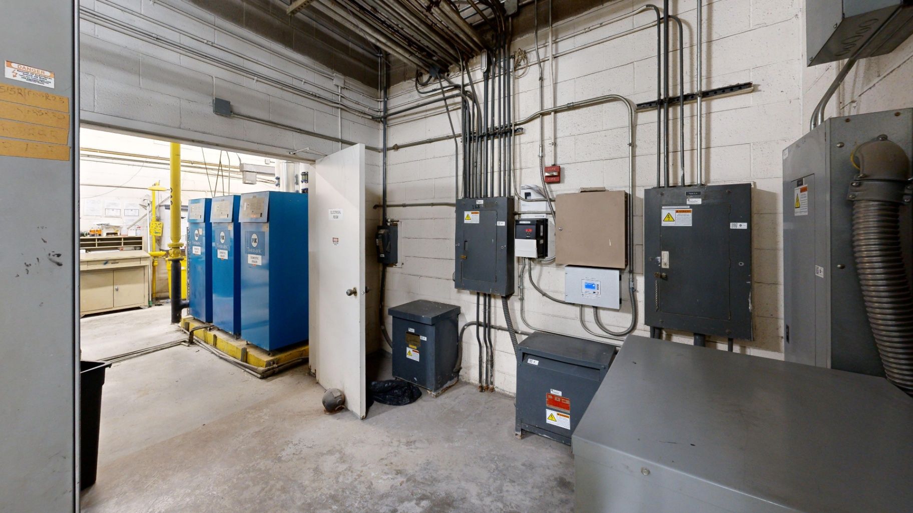 Electrical panels, conduits, adjacent equipment, and doorway inside a facility